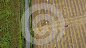 Aerial view of haymaking processed into round bales. Red tractor works in the field. On the side of the field is the