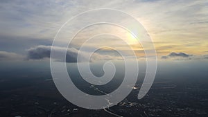 Aerial view from high altitude of distant city covered with puffy cumulus clouds flying by before rainstorm at sunset