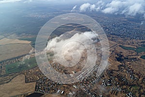 Aerial view from high altitude of distant city covered with puffy cumulus clouds forming before rainstorm. Airplane