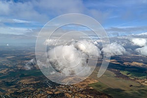 Aerial view from high altitude of distant city covered with puffy cumulus clouds forming before rainstorm. Airplane