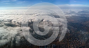 Aerial view from high altitude of distant city covered with puffy cumulus clouds forming before rainstorm. Airplane