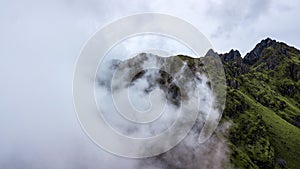 Aerial view of high green mountains rocky peaks covered with fog and clouds