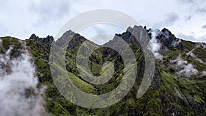 Aerial view of high green mountains rocky peaks covered with fog and clouds