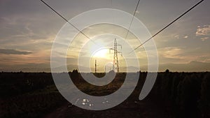 Aerial view of high voltage pylons and wires in the sky at sunset in the countryside.