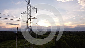 Aerial view of high voltage pylons and wires in the sky at sunset in the countryside. Drone footage of electric poles and wires at