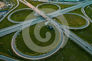 Aerial view at highway intersection or road junction with circle movement at sunset, cars and trucks traffic