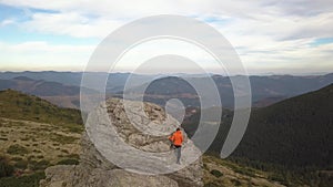 Aerial view of a hikers man and his child son climbing together on a big rock in mountains.