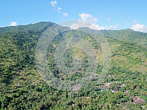 Aerial view of hills above Amed village in Bali. Hillsides densely covered with tropical vegetation and jungle. Houses of