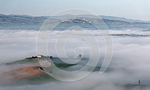 Aerial view of hilltop farmhouses & cypress trees in Tuscany on a foggy spring morning