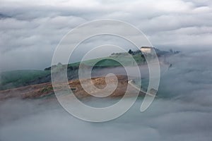 Aerial view of hilltop farmhouses & cypress trees in Tuscany on a foggy spring morning ~