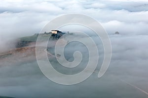 Aerial view of hilltop farmhouses & cypress trees in Tuscany on a foggy spring morning ~