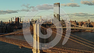 Aerial view of historic cable stayed bridge over river. Brooklyn Bridge and cityscape in background lit by late