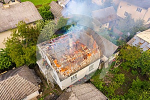 Aerial view of a house on fire with orange flames and white thick smoke