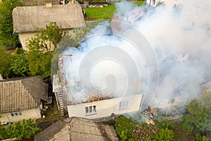 Aerial view of a house on fire with orange flames and white thick smoke