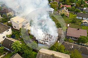 Aerial view of a house on fire with orange flames and white thick smoke