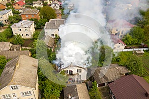 Aerial view of a house on fire with orange flames and white thick smoke