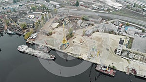 Aerial view of industrial part of the city with cargo cranes and a pile of sand with barge parked on the bank of the river. Indust