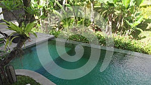 Aerial View of Infinity pool on villa with tropic garden. Woman walking on edge of pool and enjoy jungle view wearing