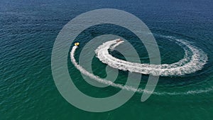 Aerial view of inflatable towed tubes to roll tourists on a tube tied to jetski across the azure sea on a sunny day