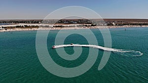 Aerial view of inflatable towed tubes to roll tourists on a tube tied to jetski across the azure sea on a sunny day