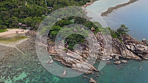Aerial view of island beach with bungalow and rocky coastline at Haad Khom beach