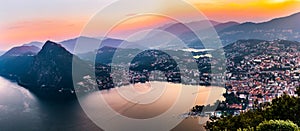 Aerial view of the lake Lugano surrounded by mountains and evening city Lugano on during dramatic sunset, Switzerland, Alps.