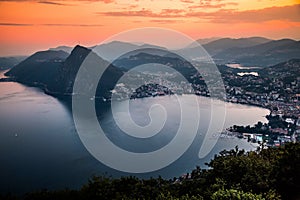 Aerial view of the lake Lugano surrounded by mountains and evening city Lugano on during dramatic sunset, Switzerland, Alps.