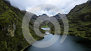 Aerial view of the lake surrounded by green mountains on cloudy day