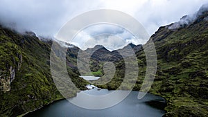 Aerial view of the lake surrounded by green mountains on cloudy day