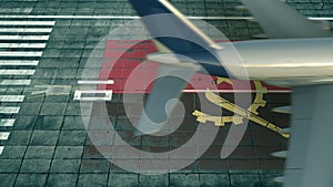 Aerial view of a landing airliner and flag of Angola on the airfield of an airport. Air travel related conceptual 3D