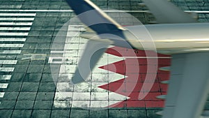 Aerial view of a landing airplane and flag of Bahrain on the airfield of an airport. Air travel related conceptual 3D