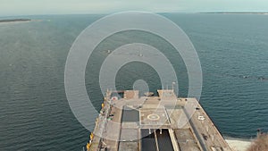 Aerial view of large gray pier with helicopter pad and walking people against blue cloudy sky and sea water in early