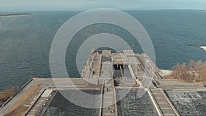 Aerial view of large gray pier with helicopter pad and walking people against blue cloudy sky and sea water in early