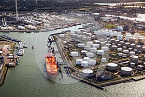 Aerial view of a large orange oil tanker moored at an oil storage silo terminal in an industrial port