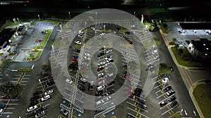 Aerial view of large parking lot at nighttime with many parked cars. Dark carpark at supercenter shopping mall with