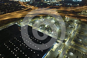 Aerial view of large parking lot at nighttime with many parked cars. Dark carpark at supercenter shopping mall with