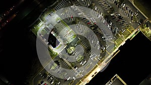 Aerial view of large parking lot at nighttime with many parked cars. Dark carpark at supercenter shopping mall with