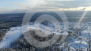 Aerial view of the large ski resort, slopes and skiing lodges surrounded by forest in winter against blue cloudy sky