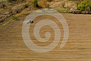 Aerial view large tractor cultivating a dry field. Top down aerial view tractor cultivating ground and seeding a dry field. Aerial