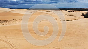 Aerial view large white sand dunes with offroad vehicle tracks, low scrub vegetation, sunny cloud blue sky, scenic desert-like