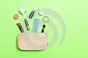 Aerial view of a leather cosmetics bag with make up beauty products spilling out on green background. Beautiful skin concept with