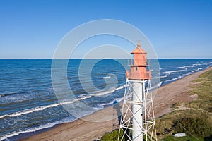 Aerial view of lighthouse with red top and white base. Blue sky and sea. Pape lighthouse