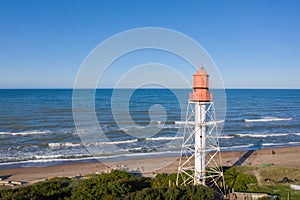 Aerial view of lighthouse with red top and white base. Blue sky and sea. Pape lighthouse