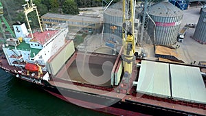 Aerial view of loading of dry cargo ship of wheat by cranes in port for import of transportation on water.