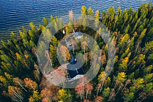 Aerial view of log cabin in autumn colors forest by blue lake in rural fall