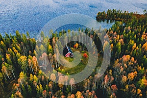 Aerial view of log cabin in autumn colors forest by blue lake in rural fall