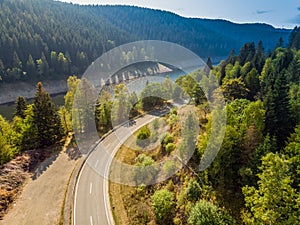 Aerial view of a lonely asphalted country road in the Harz Mountains with a neighbouring forest and the basin of a dam