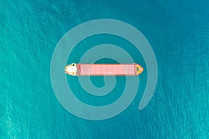 Aerial view of a lonely container ship sailing at blue sea water background. Water transportation and logistics concept. Red boat