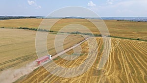 Aerial view of lorry cargo truck driving on dirt road between agricultural wheat fields. Transportation of grain after