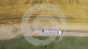 Aerial view of lorry cargo truck driving on dirt road between agricultural wheat fields. Transportation of grain after